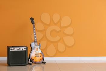 Modern guitar and amplifier near color wall�