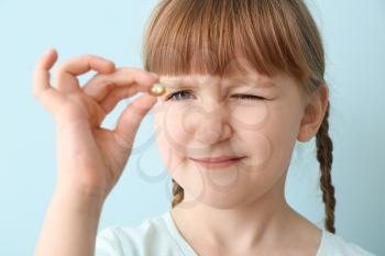 Little girl with fish oil pill on color background�