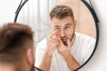 Young man putting in contact lenses near mirror�