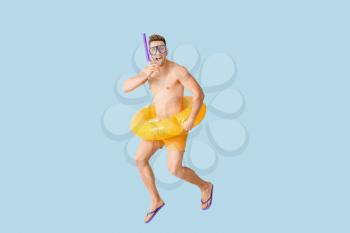 Jumping young man with inflatable ring, snorkeling mask and tube on color background�