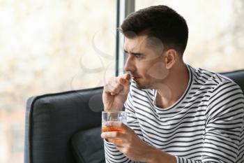 Depressed young man drinking alcohol at home�