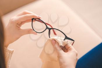 Young woman wiping eyeglasses at home, closeup�