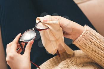 Young woman wiping eyeglasses at home, closeup�