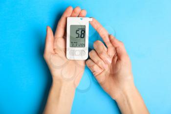 Hands of diabetic woman with digital glucometer on color background�