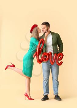 Happy young couple with air balloon in shape of word LOVE on color background�
