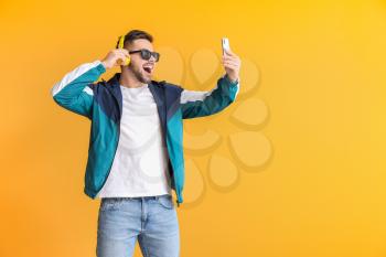 Young man with mobile phone and headphones on color background�