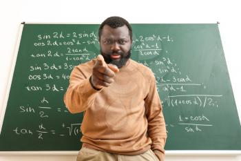 Angry African-American math teacher near blackboard in classroom�