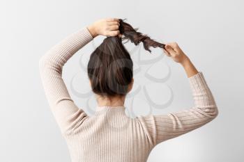 Young woman doing her hair on light background�