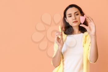 Young woman with menstrual cup and tampon on color background�