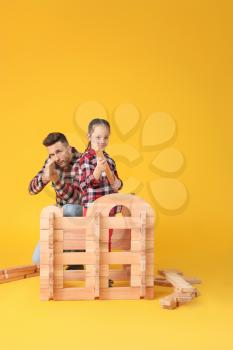 Father and little daughter playing with take-apart house on color background�