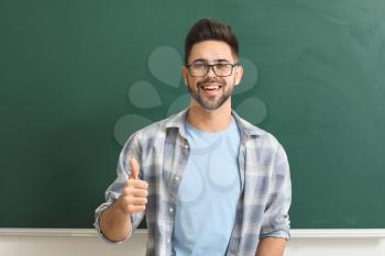 Male teacher showing thumb-up near blackboard in classroom�