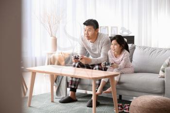 Asian man and his little daughter playing video game at home�