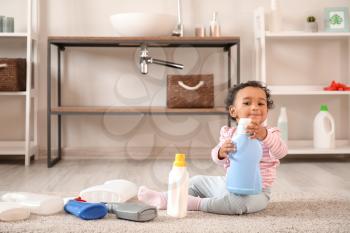 Little African-American baby playing with washing liquids at home. Child in danger�