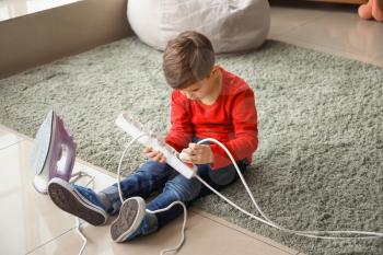 Little boy playing with electric extension cord and iron at home�