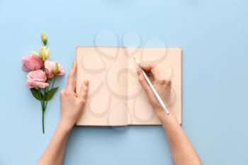 Woman writing something in notebook on color background�