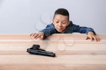 Little African-American boy playing with gun at table. Child in danger�