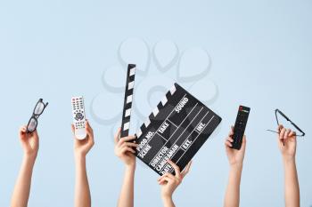 Many hands with remote controls, movie clapper and eyeglasses on color background�
