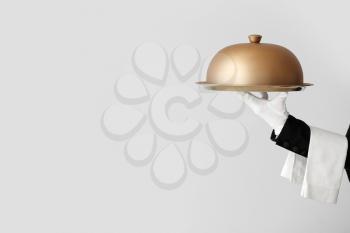 Hand of waiter with tray and cloche on grey background�