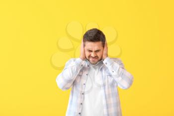 Young man suffering from loud noise on color background�