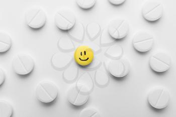 One yellow pill with drawn happy face among white ones, top view�