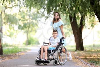 Teenage boy in wheelchair with his mother outdoors�