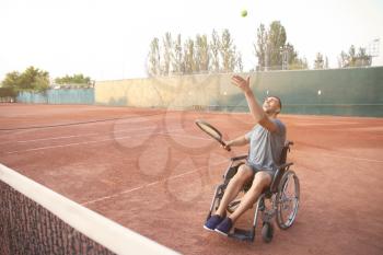 Young man in wheelchair playing tennis on court�