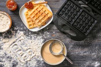 Modern waffle maker with ingredients on wooden table�