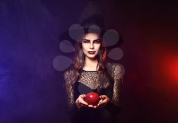 Beautiful woman dressed as witch for Halloween with apple on dark color background�