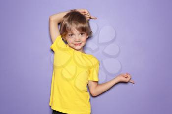 Little boy in t-shirt pointing at something on color background�