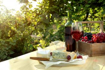 Glass and bottle of red wine with cheese on table in vineyard�