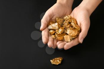 Female hands with gold nuggets on black background�