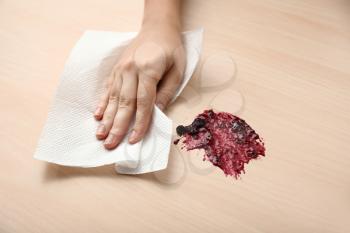 Woman wiping spot of jam on wooden table with paper towel�