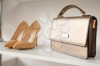 Stylish female shoes and bag on shelf in wardrobe�