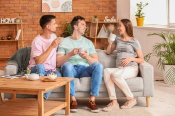 Gay couple with pregnant woman drinking tea at home�