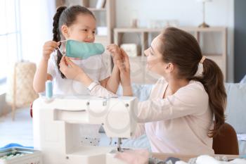 Little daughter with her mother sewing protective masks at home�