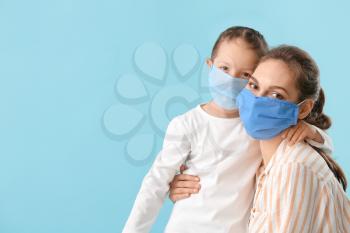 Little daughter with her mother in protective masks on color background 