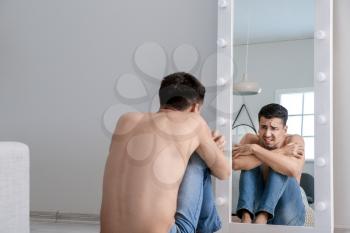 Young man with anorexia looking on his reflection in mirror at home�