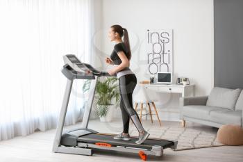 Sporty young woman training on treadmill at home 