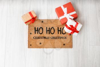 Door mat with Christmas greeting and gift boxes on wooden floor�
