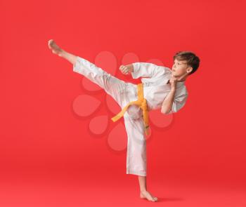Cute little boy practicing karate on color background�