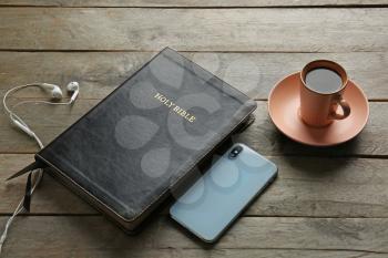 Holy Bible, tea, mobile phone and earphones on wooden background�