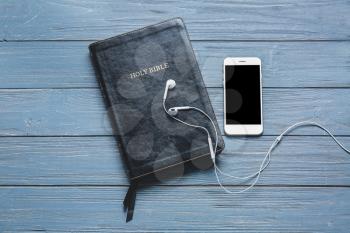 Holy Bible, mobile phone and earphones on wooden background�