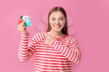 Young woman with condoms on color background�