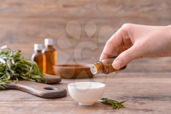 Woman dripping rosemary oil from bottle into bowl�