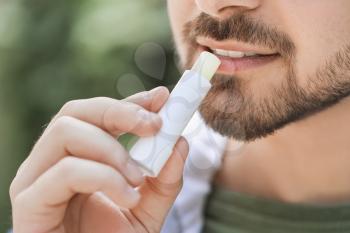 Handsome young man with lip balm outdoors, closeup�