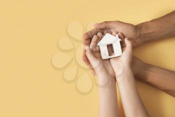 Hands of family with small house on color background�