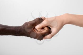 Caucasian woman and African-American man holding hands together on light background. Racism concept�