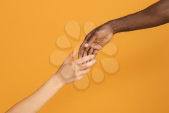 Hands of Caucasian woman and African-American man reaching out to each other on color background. Racism concept�