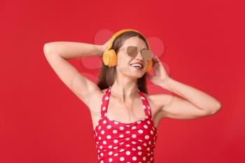 Young woman with headphones on color background�