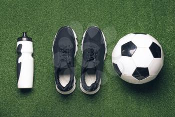 Sportive shoes, soccer ball and bottle of water on color background�